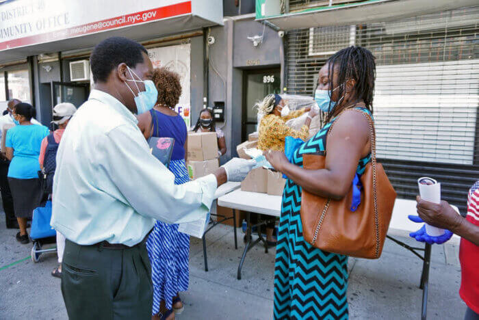 Council Member Dr. Mathieu Eugene provides a constituent with a mask to encourage her to continue to protect herself during the COVID-19 pandemic.