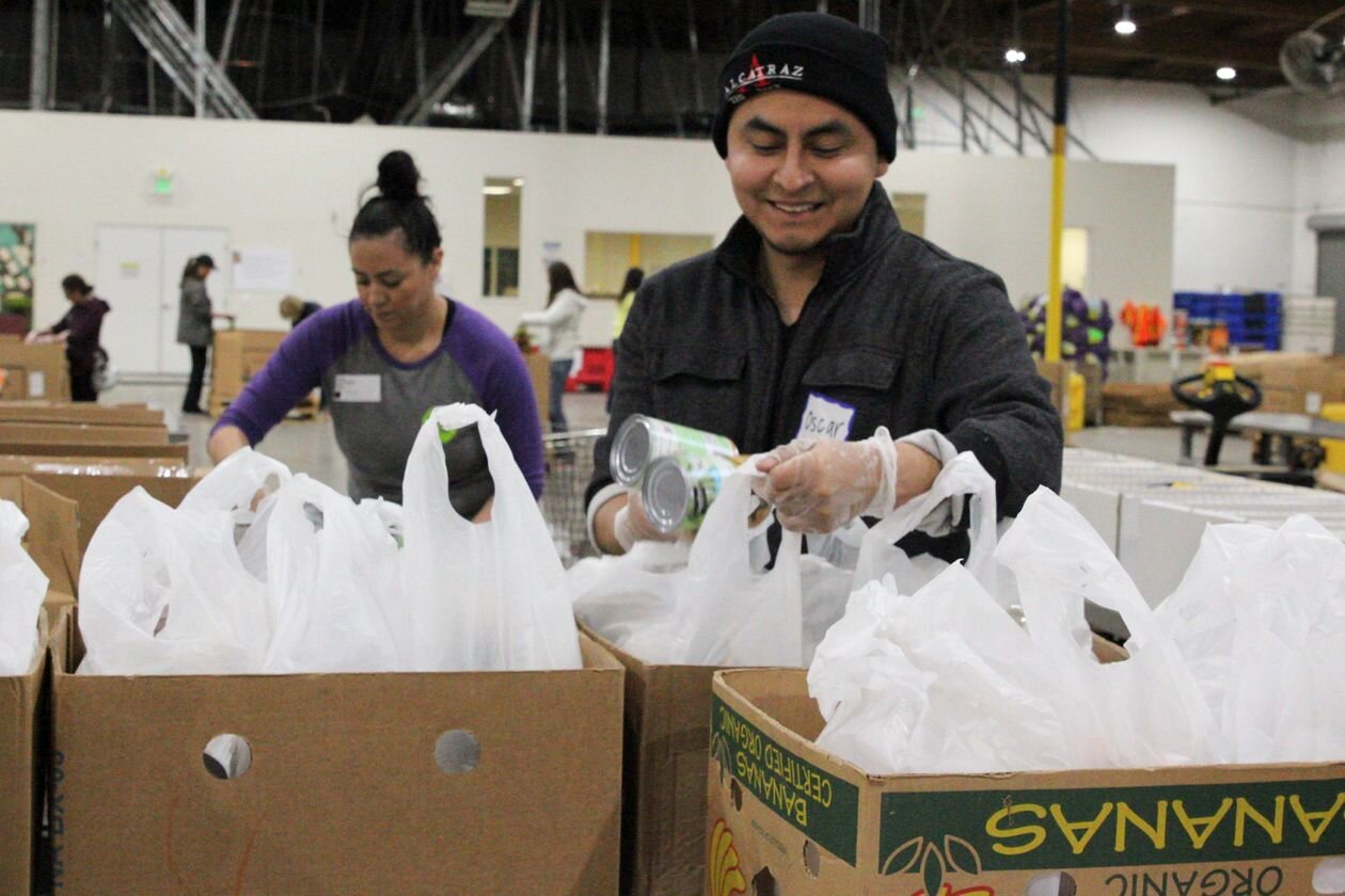 With social distancing guidelines in place, Oscar Rosas, right, and other volunteers at California’s Alameda County Community Food Bank, part of the Feeding America network, have been preparing more than 2,000 emergency bags daily to serve an unprec…
