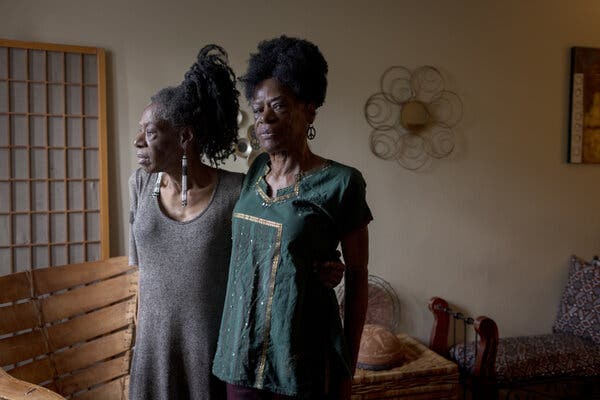 Delcina Williams and her sister Doreena Davidson stand in their living room with their arms wrapped around each other.