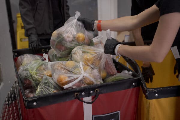 A woman grabs plastic bags of fruits and vegetables out of a red pin. She is wearing gloves.