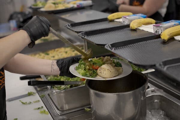 A person pours salad dressing onto a salad on a plate at a food bank.